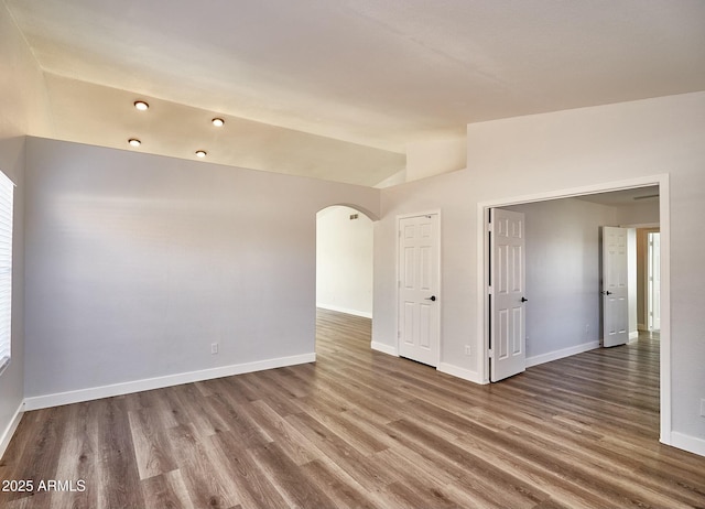 empty room with arched walkways, vaulted ceiling, baseboards, and wood finished floors