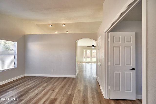 spare room featuring arched walkways, plenty of natural light, wood finished floors, and baseboards