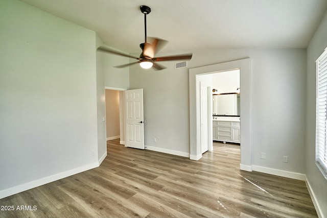 unfurnished bedroom with visible vents, baseboards, vaulted ceiling, light wood-style floors, and ensuite bath