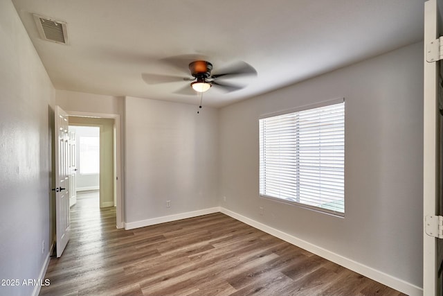 spare room featuring visible vents, ceiling fan, baseboards, and wood finished floors