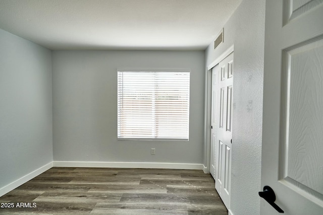 spare room with dark wood-style flooring, visible vents, and baseboards