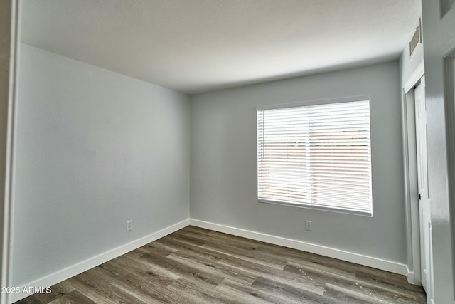 unfurnished room featuring wood finished floors, visible vents, and baseboards