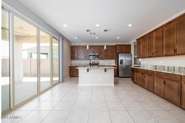 kitchen with pendant lighting, an island with sink, stainless steel appliances, and light stone countertops