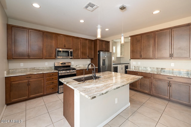 kitchen with hanging light fixtures, appliances with stainless steel finishes, light stone countertops, sink, and a center island with sink