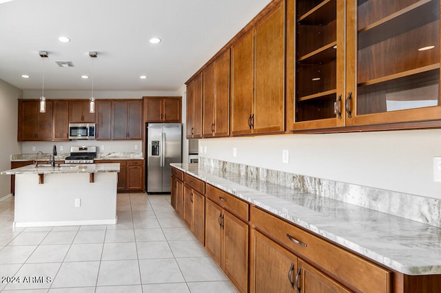 kitchen with pendant lighting, stainless steel appliances, a kitchen breakfast bar, an island with sink, and light stone countertops