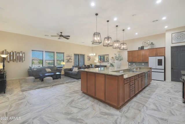 kitchen with light stone countertops, refrigerator, hanging light fixtures, a spacious island, and ceiling fan