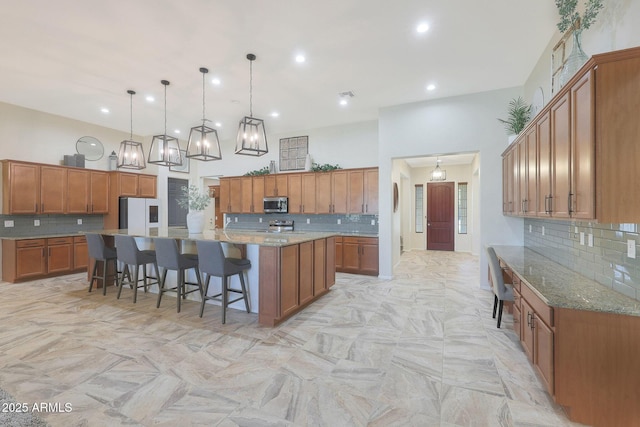 kitchen featuring a kitchen bar, refrigerator, a large island with sink, light stone countertops, and pendant lighting