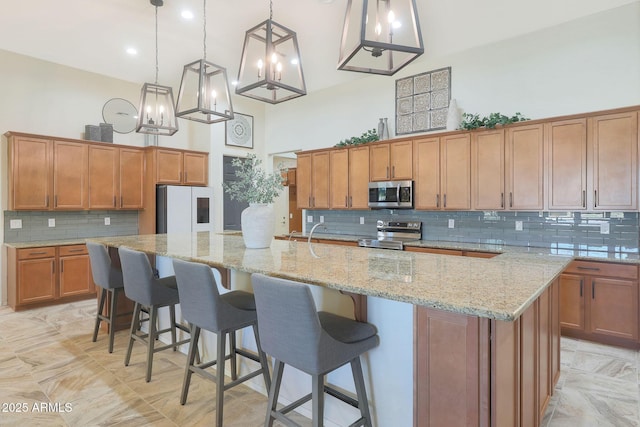 kitchen with stainless steel appliances, a towering ceiling, hanging light fixtures, and a spacious island