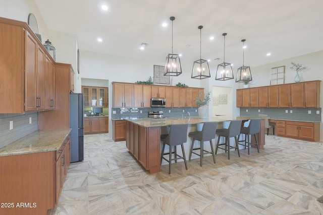 kitchen with light stone counters, pendant lighting, stainless steel appliances, a large island, and a breakfast bar area