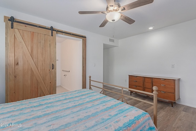 bedroom featuring connected bathroom, a barn door, hardwood / wood-style flooring, and ceiling fan