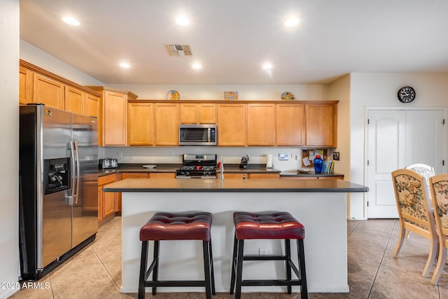 kitchen with a breakfast bar, an island with sink, stainless steel appliances, and light tile patterned floors