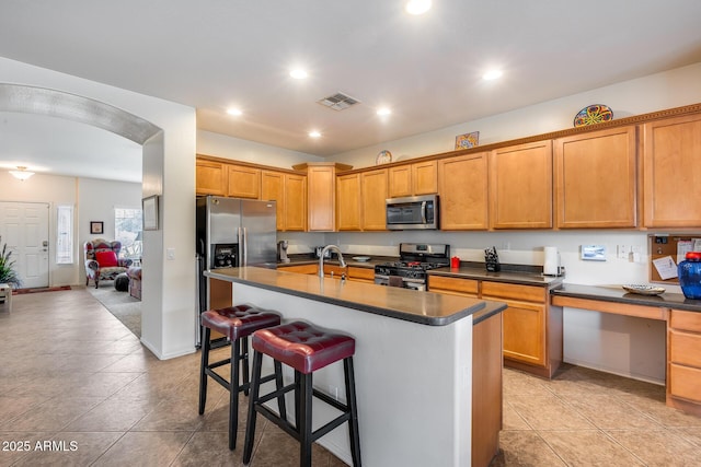 kitchen with sink, a kitchen island with sink, a breakfast bar, light tile patterned flooring, and appliances with stainless steel finishes