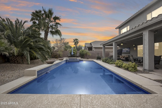 pool at dusk featuring an in ground hot tub, ceiling fan, and a patio area