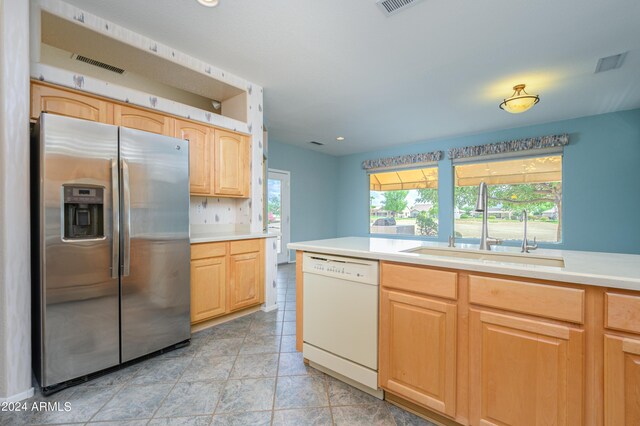 kitchen featuring sink, light tile patterned floors, white dishwasher, light brown cabinetry, and stainless steel fridge