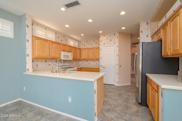 kitchen with sink, kitchen peninsula, white appliances, light tile patterned floors, and light brown cabinetry