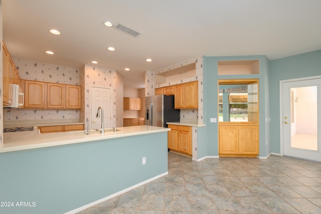 kitchen featuring appliances with stainless steel finishes, decorative backsplash, kitchen peninsula, light brown cabinets, and sink