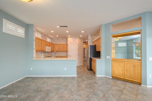 kitchen with light brown cabinets, sink, kitchen peninsula, white appliances, and backsplash