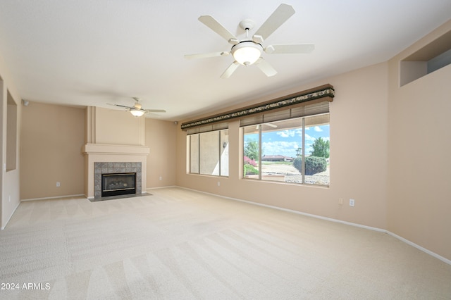 unfurnished living room with ceiling fan, a tiled fireplace, and light carpet