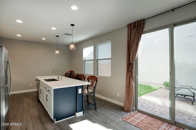 kitchen featuring white cabinets, stainless steel appliances, a center island with sink, decorative light fixtures, and dark hardwood / wood-style flooring