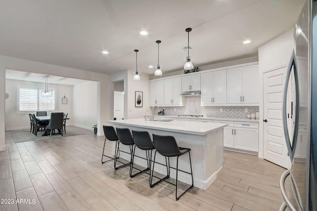 kitchen with decorative light fixtures, white cabinetry, stainless steel appliances, and a kitchen island with sink