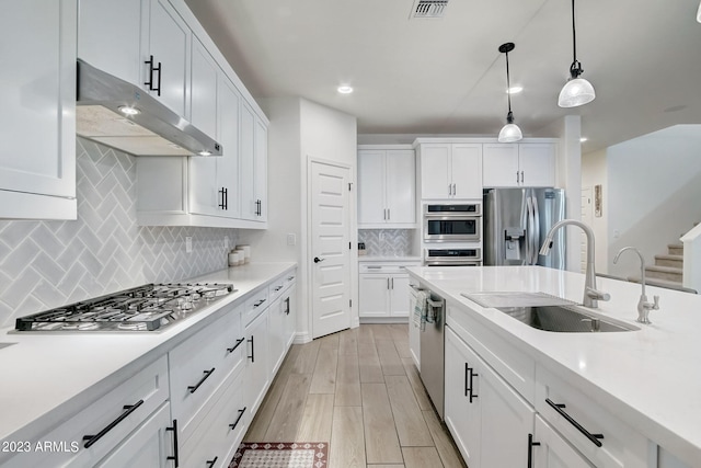 kitchen with sink, stainless steel appliances, white cabinetry, and decorative light fixtures