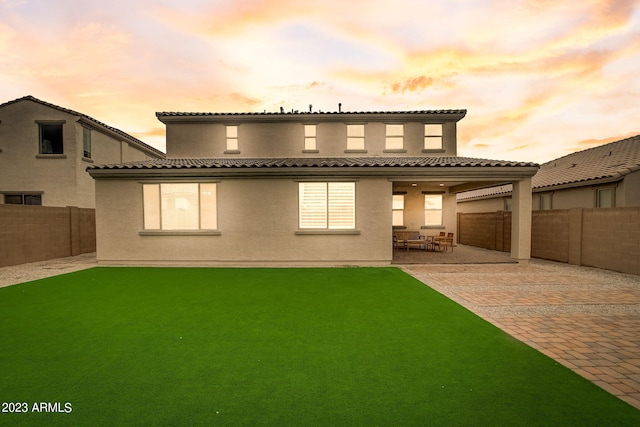 back house at dusk featuring a lawn and a patio area