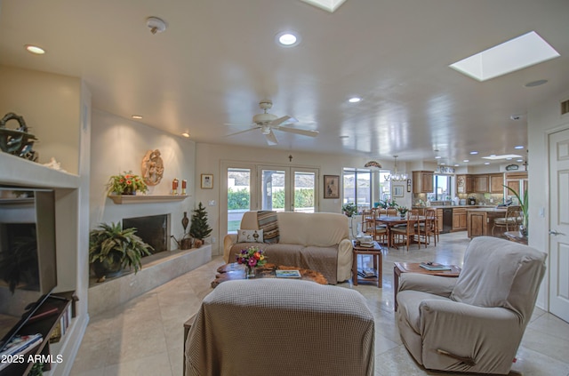 living area featuring recessed lighting, a fireplace with raised hearth, light tile patterned flooring, a skylight, and a ceiling fan