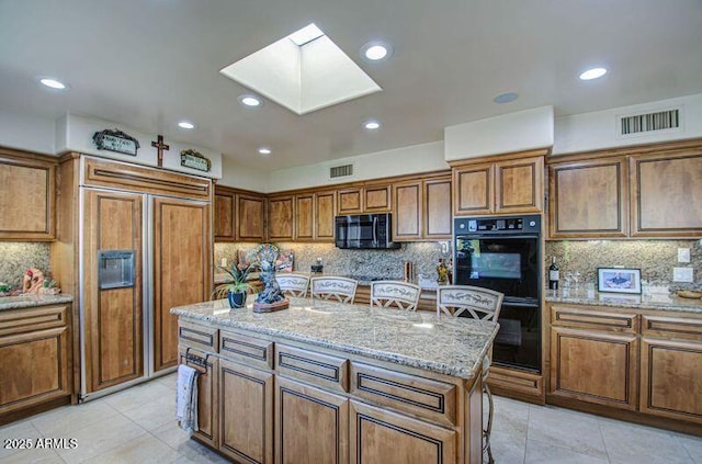 kitchen featuring dobule oven black, a skylight, brown cabinets, and paneled refrigerator