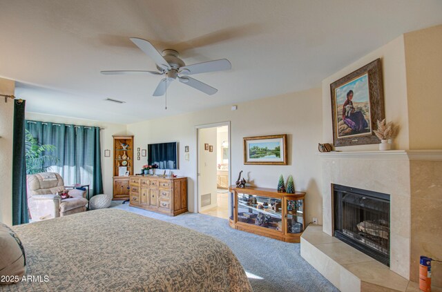 bedroom featuring visible vents, light carpet, ensuite bathroom, ceiling fan, and a tile fireplace