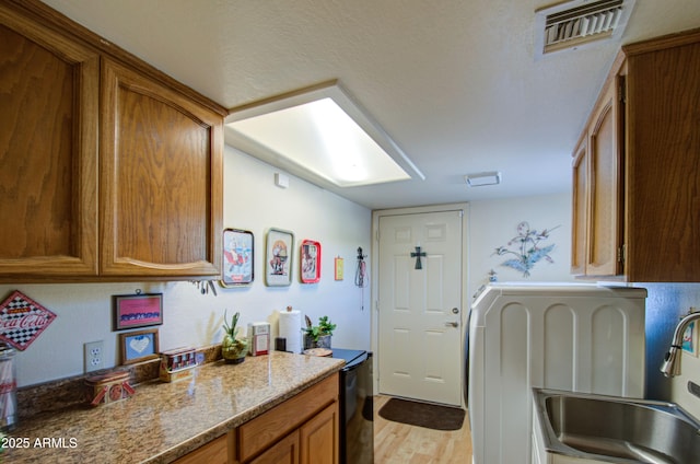 kitchen featuring visible vents, a sink, light wood-type flooring, brown cabinetry, and washer / dryer
