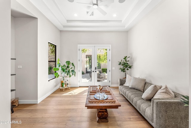 living room with french doors, a raised ceiling, and light hardwood / wood-style floors