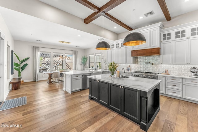 kitchen with hanging light fixtures, light wood-type flooring, beamed ceiling, and a kitchen island with sink