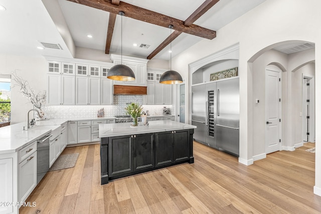 kitchen featuring decorative backsplash, pendant lighting, light hardwood / wood-style flooring, appliances with stainless steel finishes, and beam ceiling