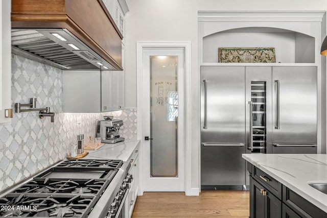 kitchen with light stone counters, white cabinets, premium range hood, high end appliances, and light wood-type flooring