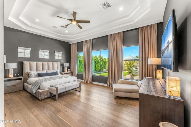 bedroom with a raised ceiling, light hardwood / wood-style floors, and ceiling fan