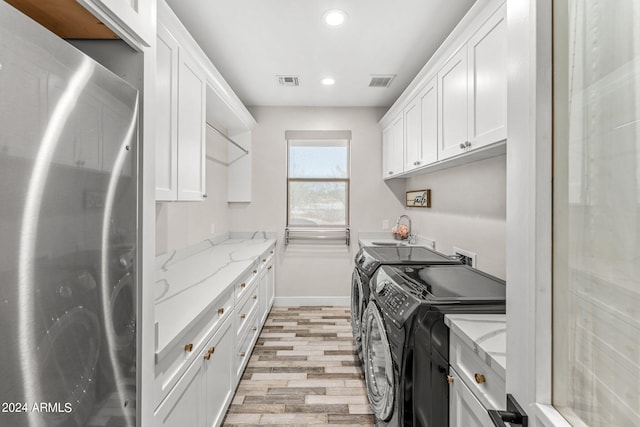 clothes washing area featuring cabinets, light hardwood / wood-style flooring, sink, and independent washer and dryer