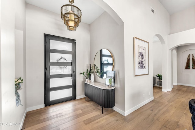 entryway featuring light wood-type flooring, a towering ceiling, and a chandelier