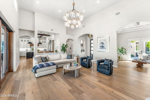 living room featuring ceiling fan with notable chandelier, french doors, a towering ceiling, and light hardwood / wood-style flooring