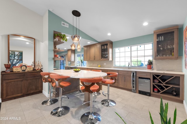 kitchen featuring backsplash, kitchen peninsula, pendant lighting, vaulted ceiling, and light tile patterned floors