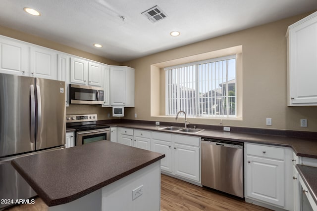 kitchen featuring white cabinets, stainless steel appliances, sink, a kitchen island, and light hardwood / wood-style floors