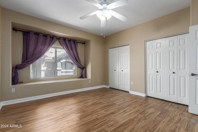 unfurnished bedroom with ceiling fan, light wood-type flooring, and multiple closets