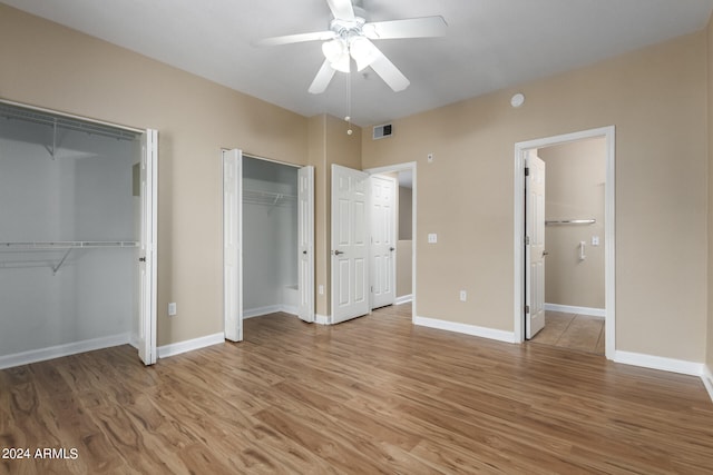 unfurnished bedroom featuring hardwood / wood-style flooring, ceiling fan, and two closets