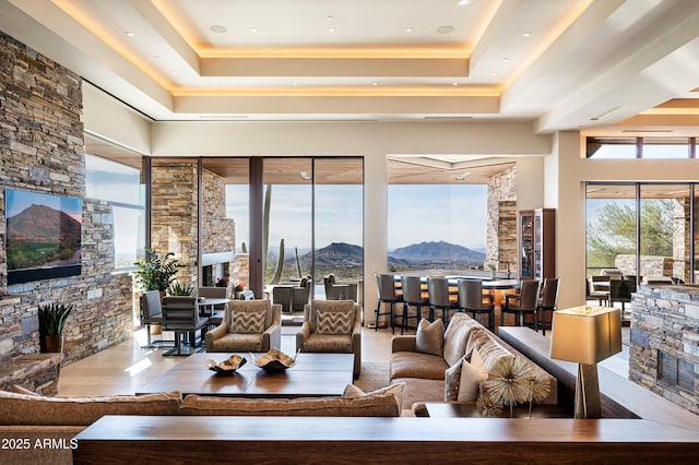 living room with a tray ceiling, a stone fireplace, and a mountain view