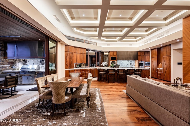 dining area featuring beam ceiling, light hardwood / wood-style flooring, and coffered ceiling