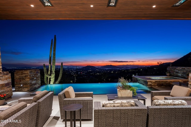 pool at dusk with an in ground hot tub, a mountain view, and an outdoor living space