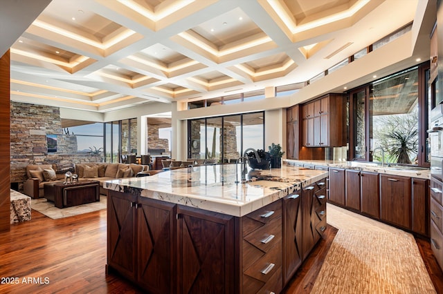 kitchen with sink, coffered ceiling, light stone counters, light hardwood / wood-style flooring, and a spacious island