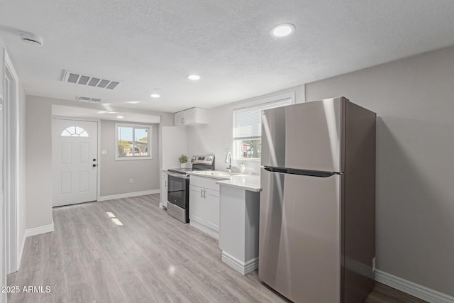 kitchen featuring sink, white cabinets, stainless steel appliances, a textured ceiling, and light hardwood / wood-style flooring