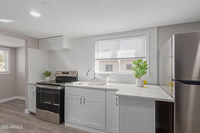 kitchen with sink, a textured ceiling, light hardwood / wood-style flooring, stainless steel appliances, and white cabinets