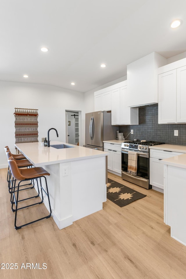 1212 E Indianola Ave, Phoenix, AZ 85014 - kitchen with stainless steel appliances, a sink, light wood-style flooring, a breakfast bar area, and white cabinetry