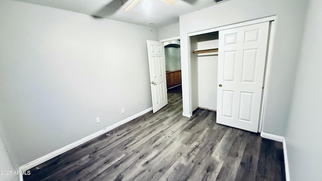 unfurnished bedroom with dark wood-style floors, baseboards, a closet, and ceiling fan